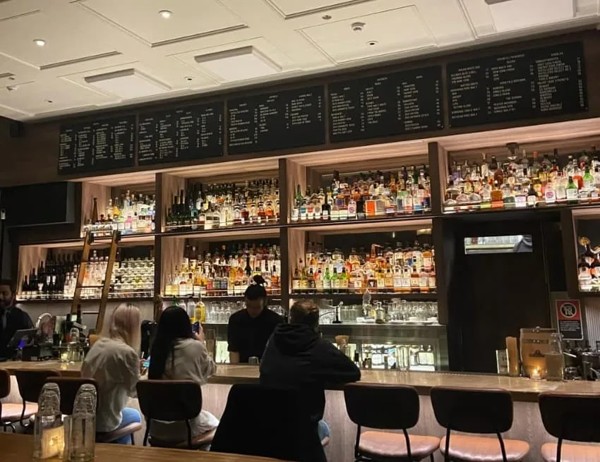 Banchō's back bar: lit shelves of whisky under chalkboard menus, with drinkers along the timber counter