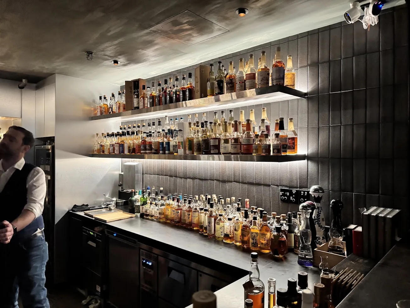 Bar Besuto's back bar: two lit steel shelves and a long counter lined with Japanese whisky bottles