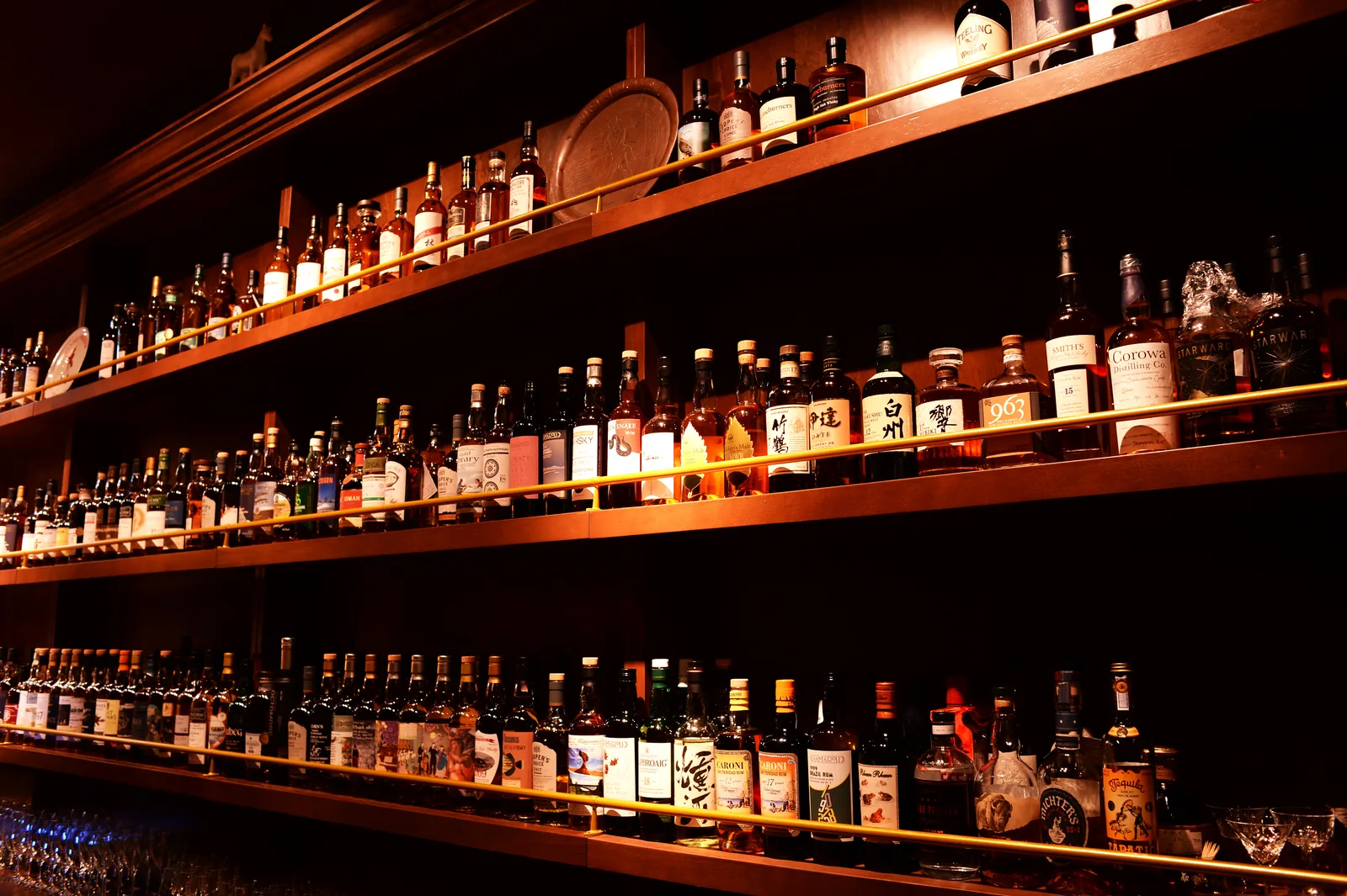 The Elysian's back bar: four lit timber shelves of whisky behind brass rails, with Hibiki, Hakushu and Taketsuru among the bottles